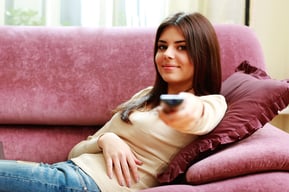 Young happy woman lying on the sofa with remote control at home